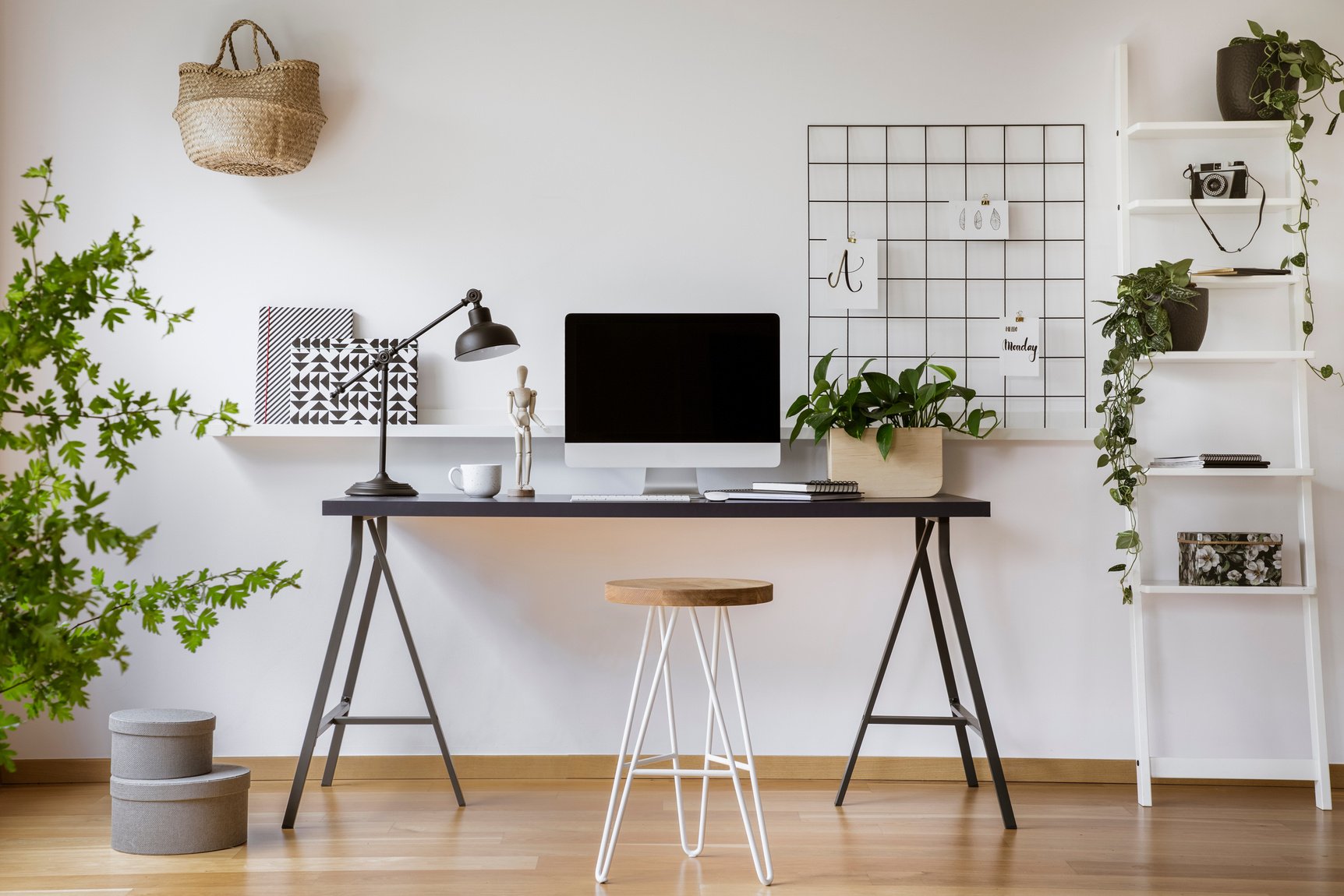 Hairpin stool standing by the wooden desk with mockup computer screen, metal lamp and coffee cup in real photo of white home office interior